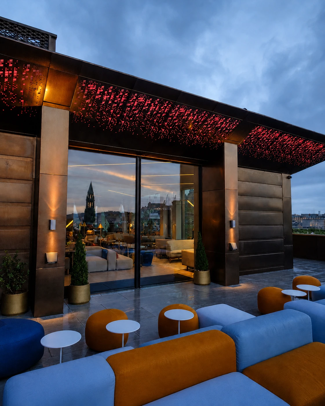 1820 Rooftop Bar’s exact terrace, with powder-blue and ochre seating, bronze planters and its dark glazed pavilion beneath an Edinburgh skyline.