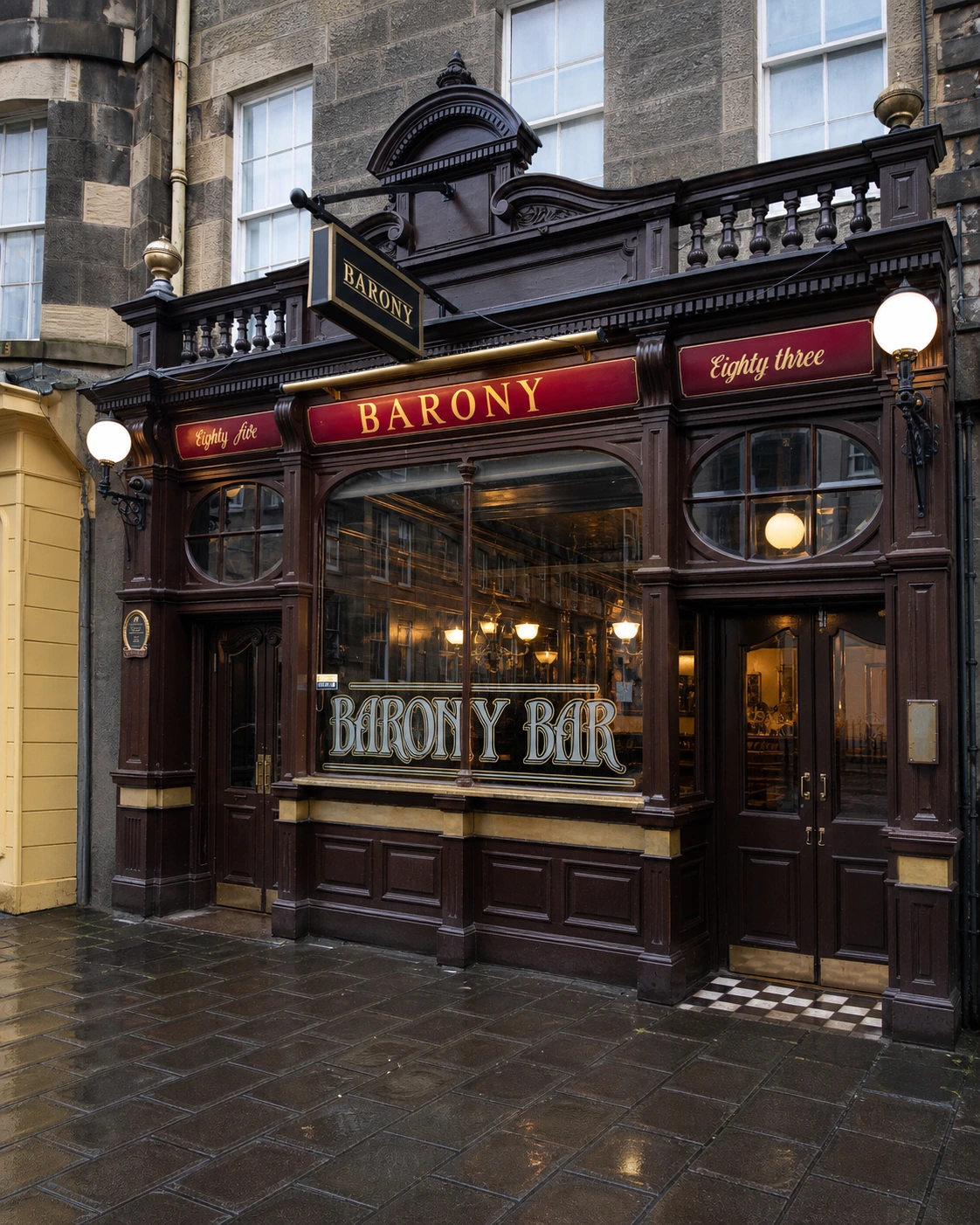 Dark carved Barony Bar shopfront, with the red BARONY fascia, BARONY BAR window lettering and doors beneath oval transoms.