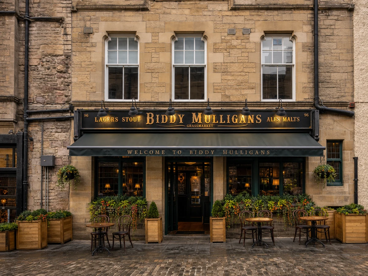 Biddy Mulligans’ Grassmarket sandstone frontage with dark green framing, black-and-gold fascia, awning and pavement seating.