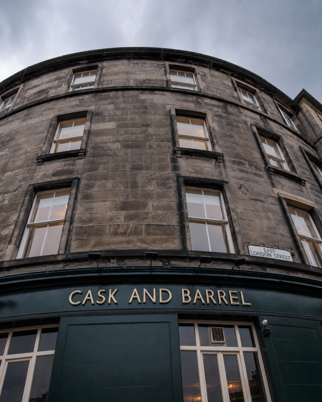 Cask & Barrel principal sign beneath the curved sandstone corner, with dark-green frontage and gold lettering.