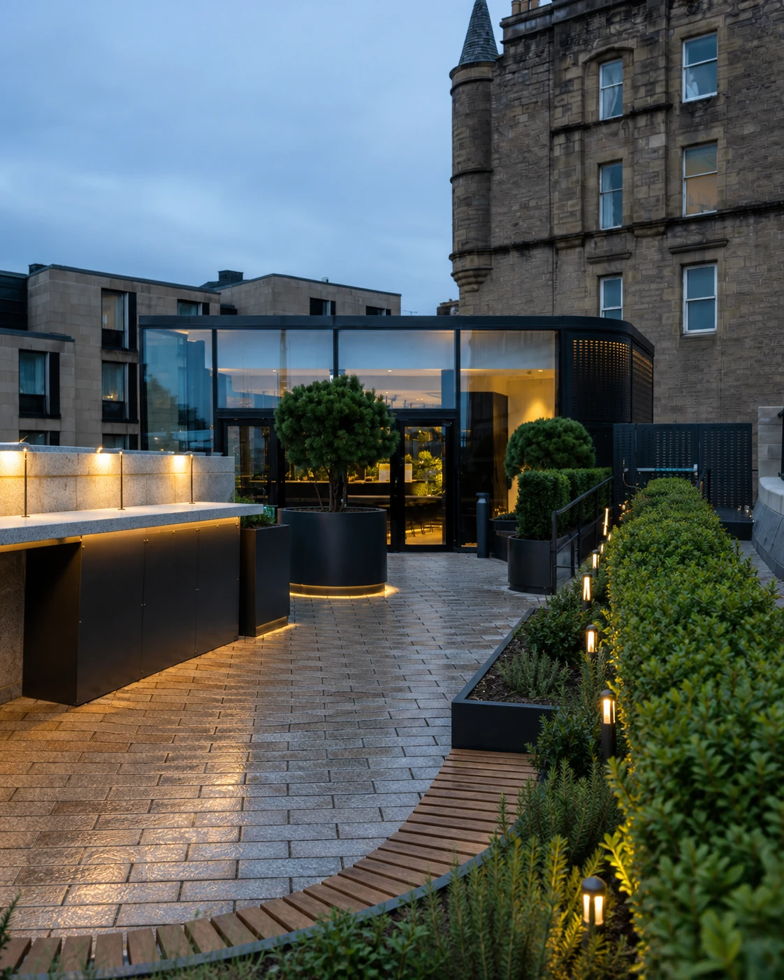 Edinburgh Gin Roof Garden Bar’s exact botanical terrace path, with clipped planting, warm paver lights and its low black-glass pavilion.