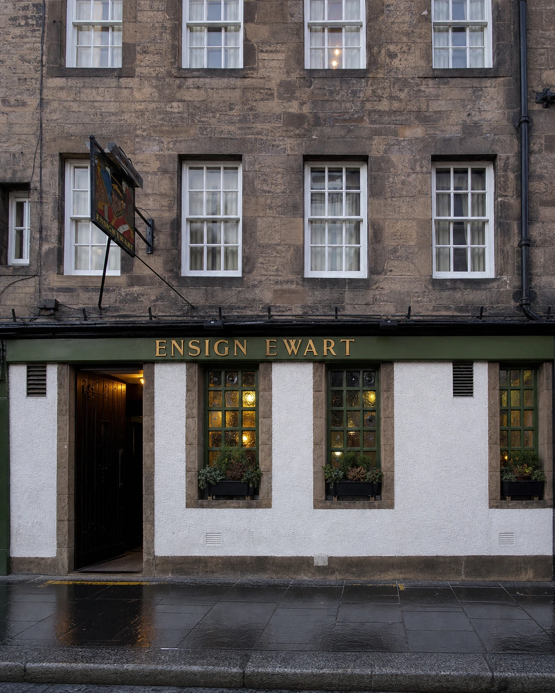 Ensign Ewart’s white-and-olive Royal Mile frontage beneath brown sandstone sash windows, with its soldier hanging sign after rain.
