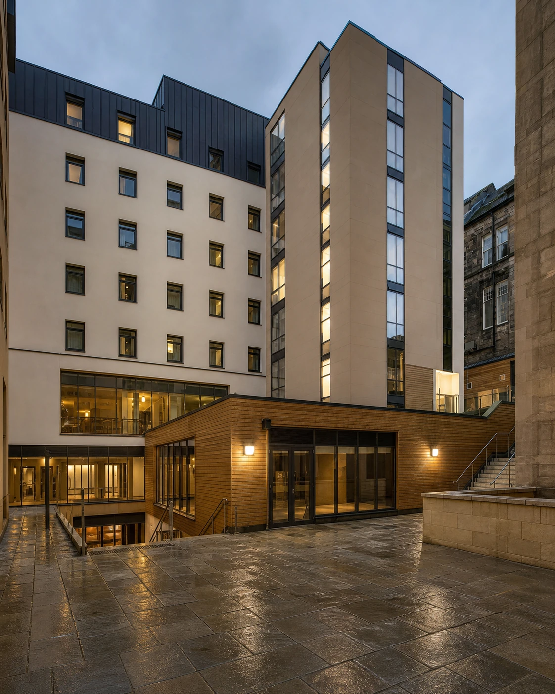 La Belle Angele’s exact rebuilt SoCo host courtyard, with pale multi-storey walls, glazed stair tower, timber pavilion and split-level steps after rain.