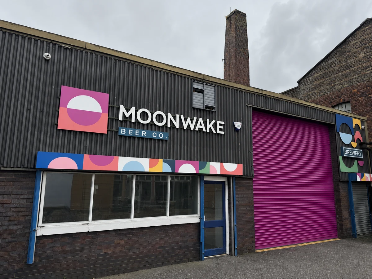Moonwake’s charcoal industrial brewery frontage with pink moon mark, white wordmark and magenta shutter.