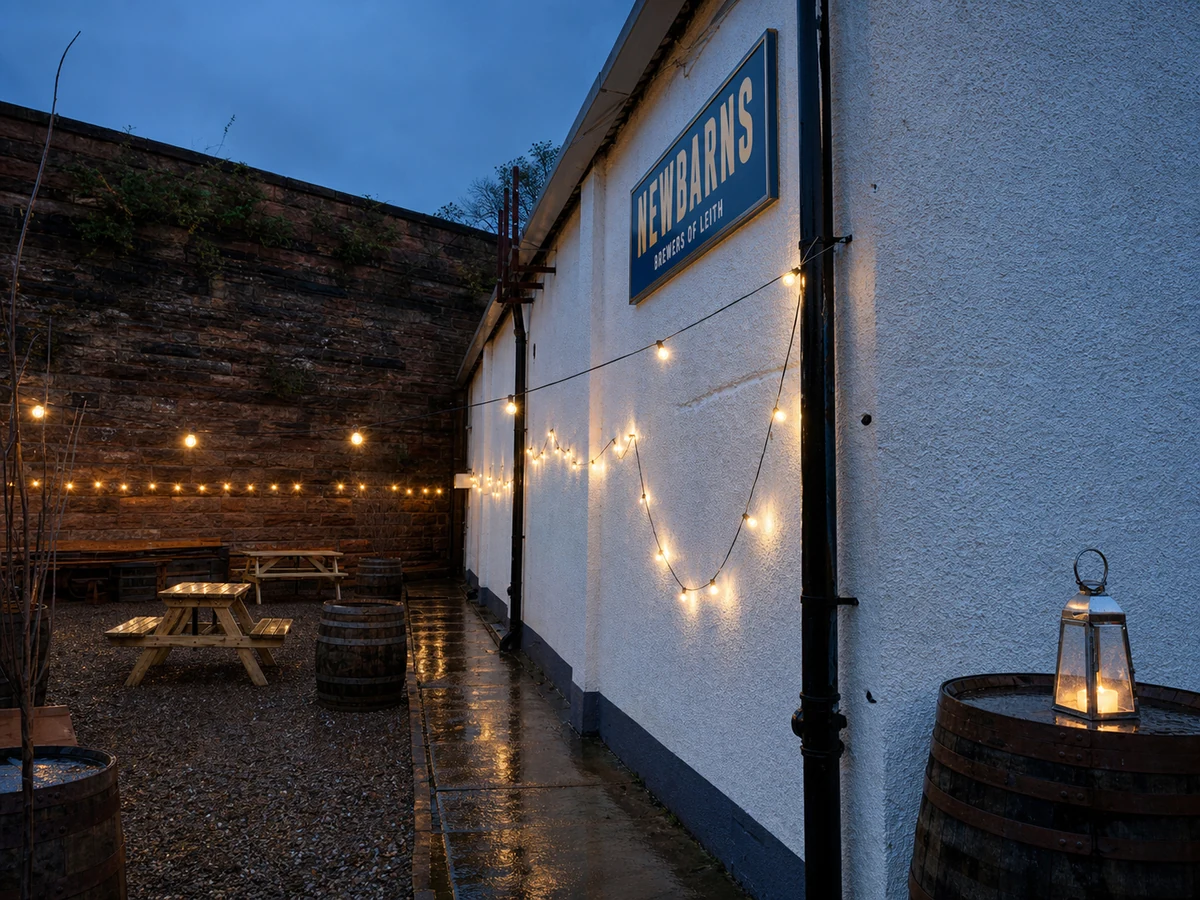 Newbarns Brewery Taproom’s source-led Jane Street courtyard: white brewery wall, old brick boundary, wet gravel, string lights and crisp “NEWBARNS – BREWERS OF LEITH” sign.