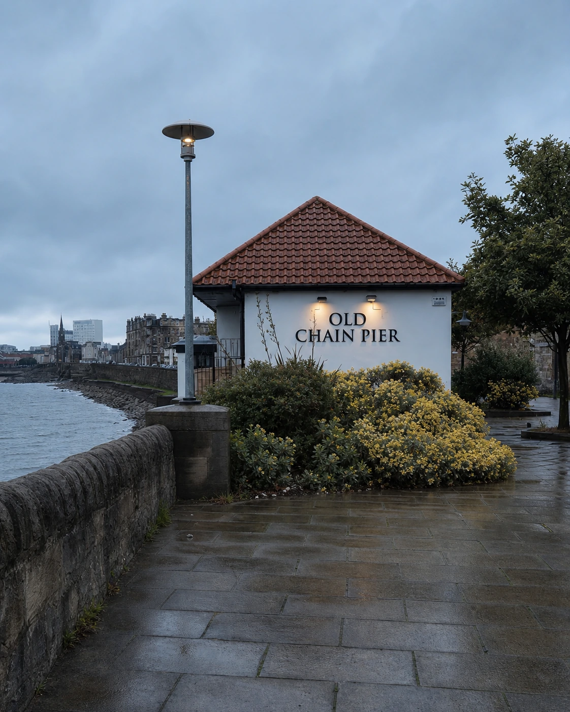 White OLD CHAIN PIER waterfront end wall and hipped red-tiled roof beside the promenade and sea wall.