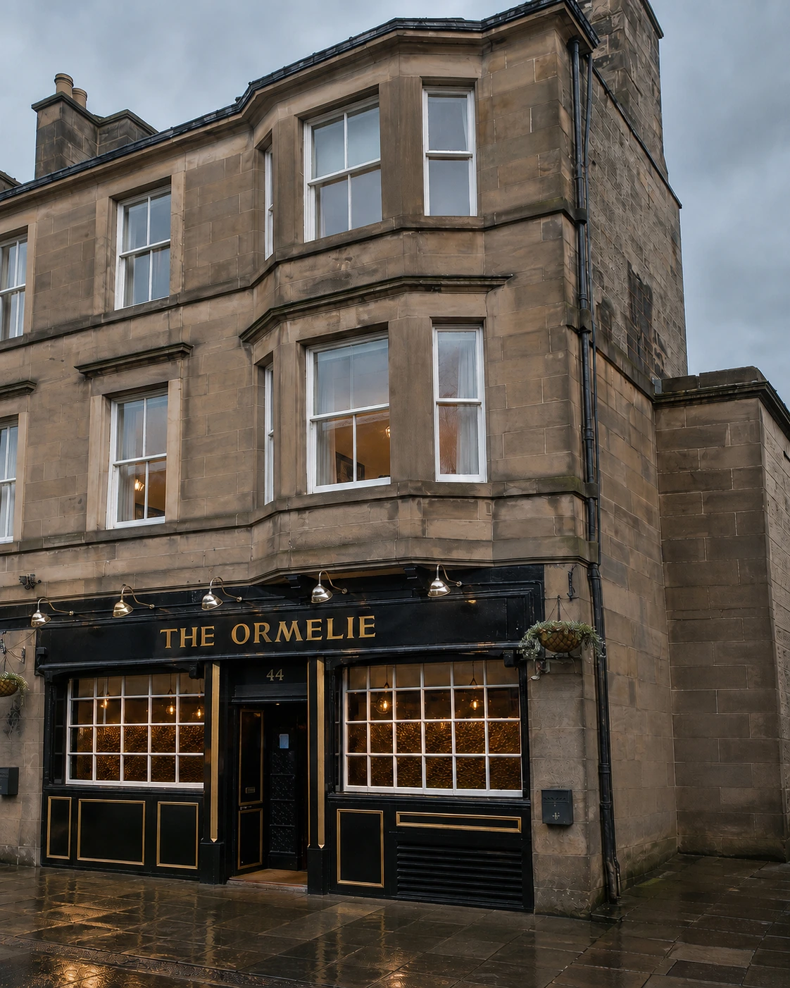 Ormelie Tavern with black and gold frontage, central door and two broad windows below its sandstone bay.