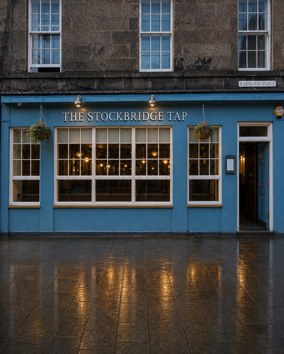 The Stockbridge Tap’s blue Raeburn Place frontage, broad white windows and right-hand door after rain.