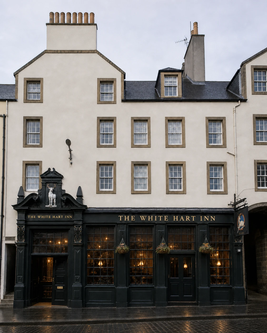 The White Hart Inn’s charcoal-green Grassmarket frontage with gold name, ornate white-stag pediment and cream sash-window tenement after rain.